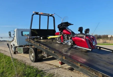 Red motorcycle strapped down on a white flatbed tow truck